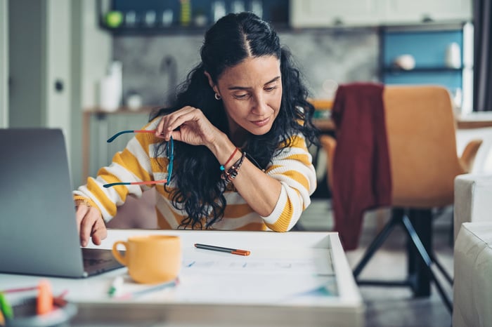 A person studies a paper document while sitting at a laptop.