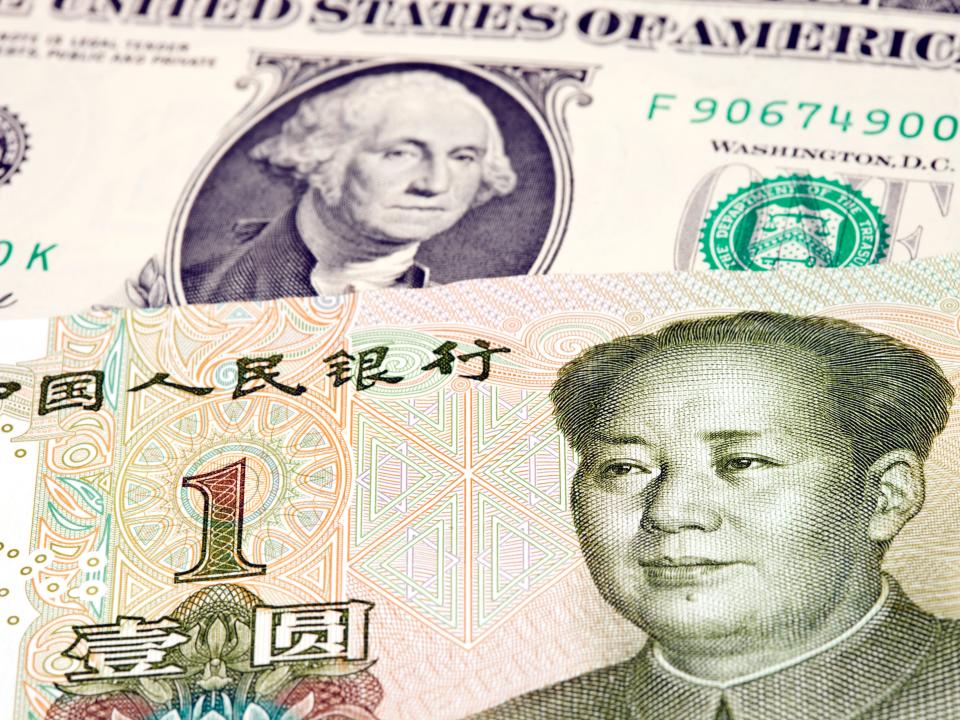 One Chinese yuan bill lying on top of a US dollar bill.