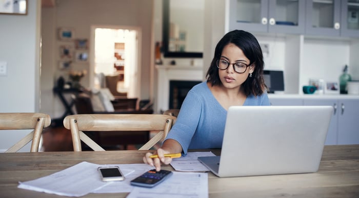 A person working on a table with a laptop and pieces of paper.