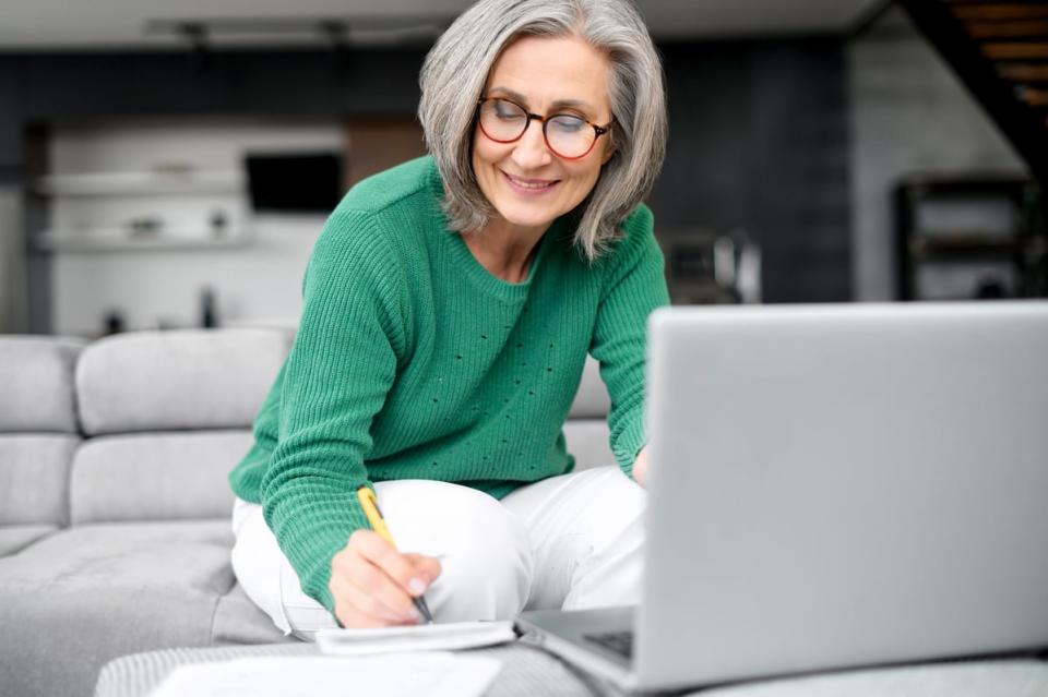 A person writes on a notepad while sitting in front of a laptop computer.