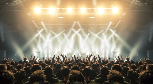 A crowd with hands in the air backlit by stage lights at a concert.