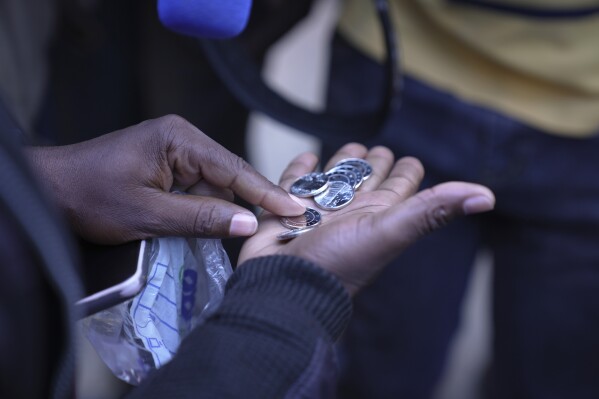 A woman shows the new Zimbabwean bank coins called the ZiG, in the streets of Harare, Zimbabwe, Tuesday, April 30, 2024. Zimbabwe started circulating banknotes and coins for another new currency Tuesday in its latest attempt to solve a long-running and at times baffling monetary crisis that has seen the government try gold coins and a digital currency among other ideas. (AP Photo/Tsvangirayi Mukwazhi)