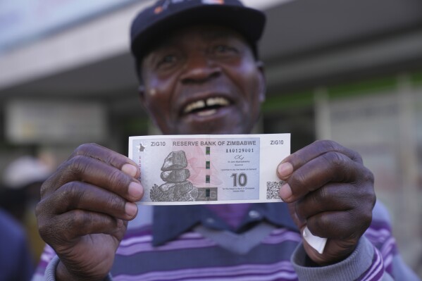 A man smiles while holding the new Zimbabwean banknote, called the ZiG, in the streets of Harare, Zimbabwe, Tuesday, April 30, 2024. Zimbabwe started circulating banknotes and coins for another new currency Tuesday in its latest attempt to solve a long-running and at times baffling monetary crisis that has seen the government try gold coins and a digital currency among other ideas. (AP Photo/Tsvangirayi Mukwazhi)