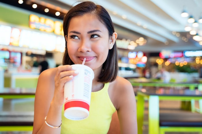 A person sips their drink through a straw while sitting in a food court.