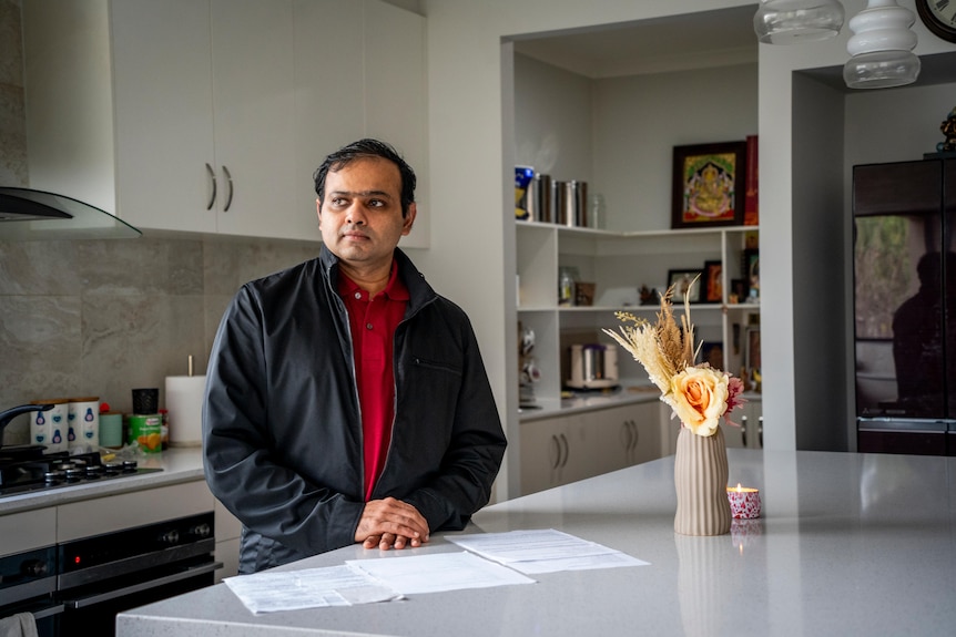 A man standing at his kitchen counter with paperwork in front of him.