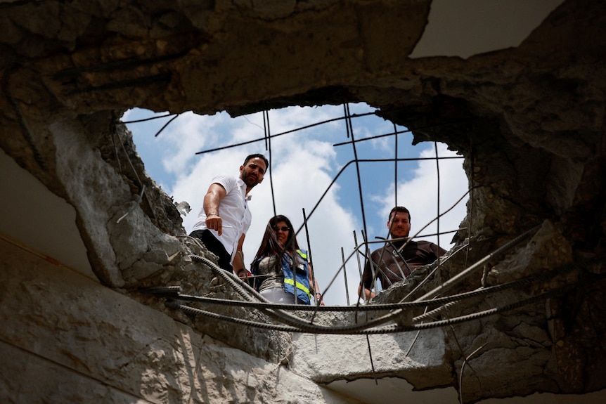 Three people look from above at damage from an explosion