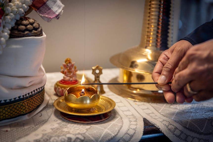 Karthik Sivasubramanian's hands are seen as he lights an oil candle in his home.