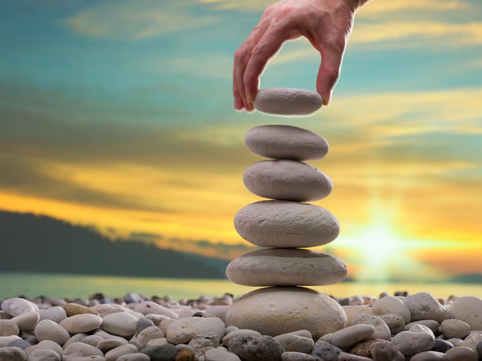 A person stacking stones in a tower with a bright sunrise in the background.