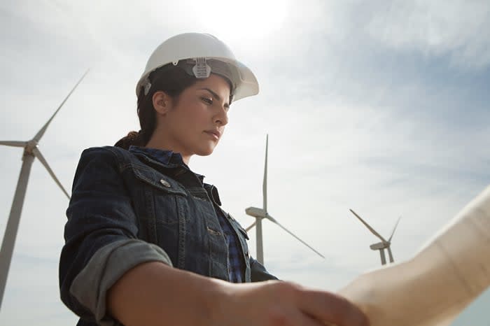 A person in work gear looking at blueprints, with wind turbines in the background.