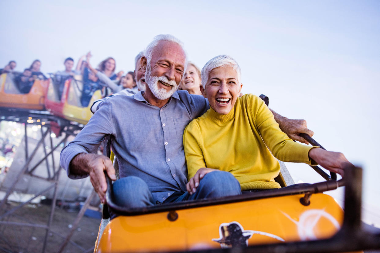 Cheerful senior couple having fun while riding on rollercoaster at amusement park. Copy space.