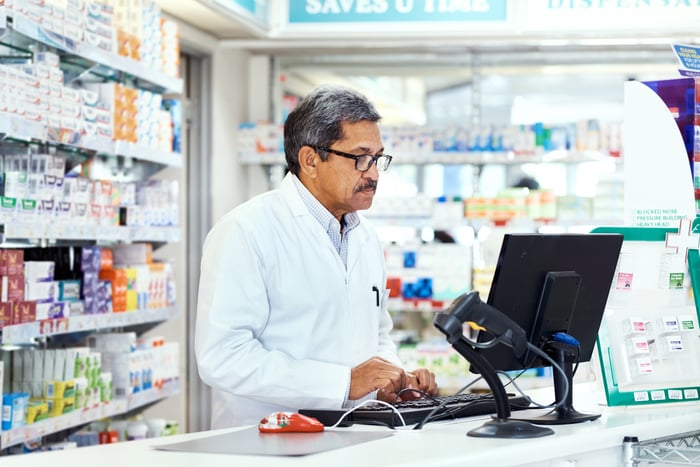 Person in white laboratory attire within a retail environment utilizing a personal computing device.