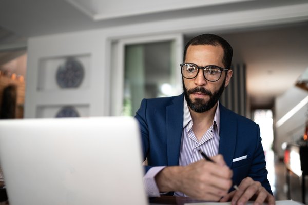 Professionally dressed individual takes notes in front of laptop.