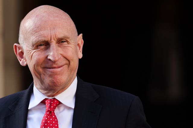 A middle aged bald man on the left of the frame wearing a red tie