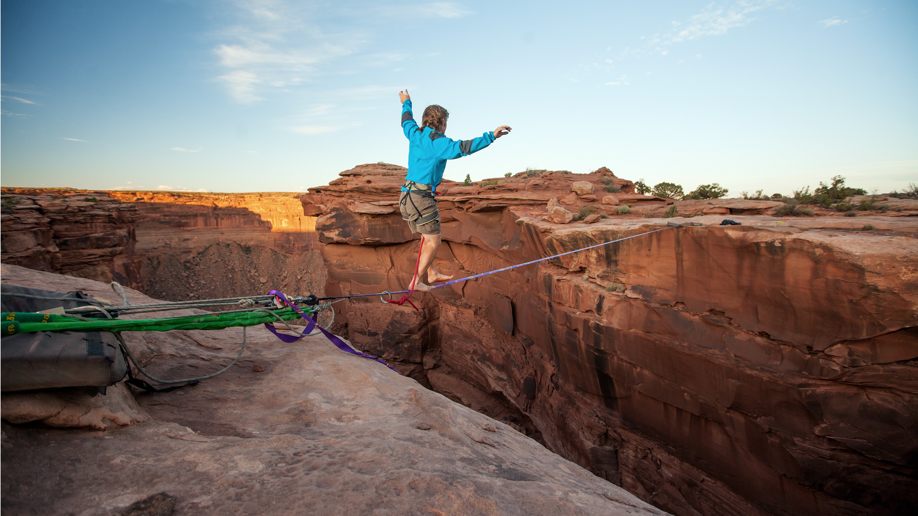A barefoot man balances on a tightrope over a mountain chasm.