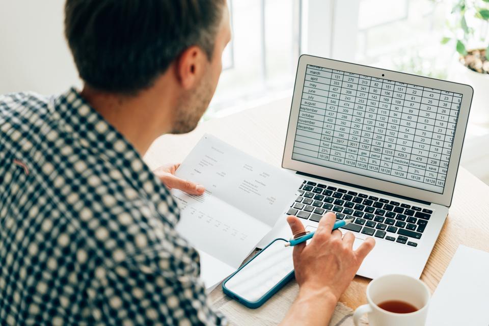 Man using calculator, analyzing financial data. Focused on  work and working on budget or expense report. Man sitting at  table in well-lit office.