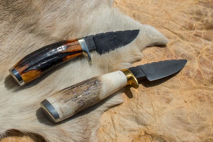 Two antler handle fixed blade Damascus knives displayed on top of a folded antler hide.