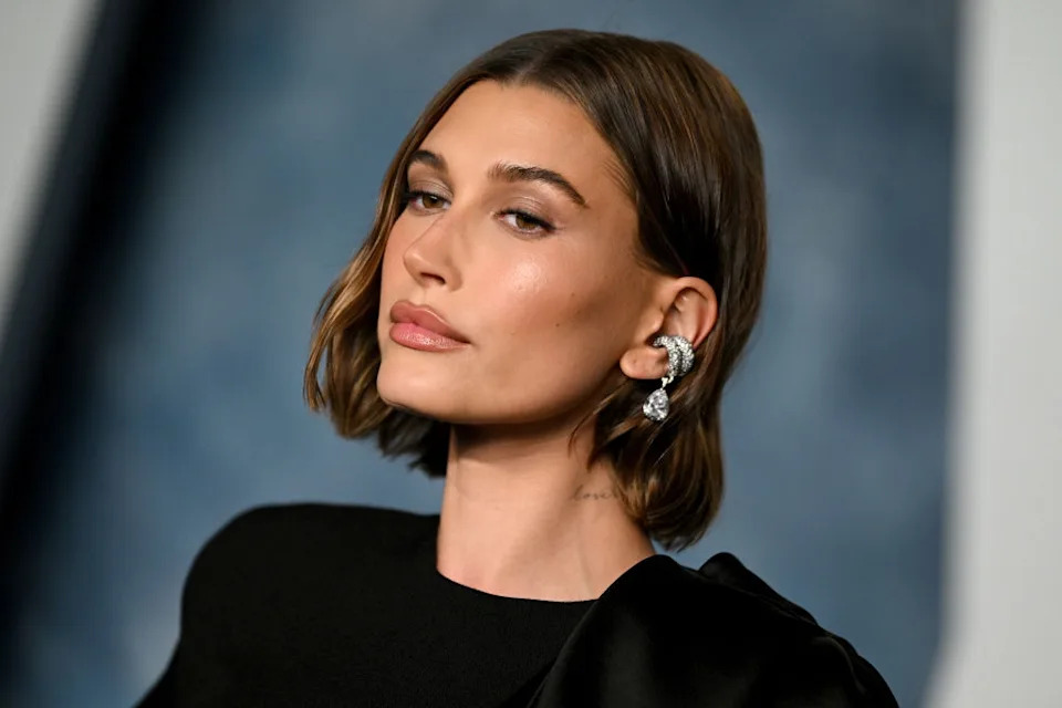 Person with sleek bob hairstyle wearing a stylish, asymmetrical black outfit, looking to the side, against a blurry background