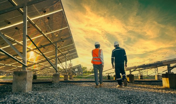 Two people walking near solar energy panels with a sunset in the background.
