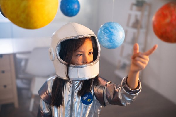 Child with a space helmet plays with a solar system model.