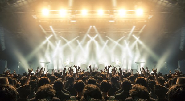 A crowd with hands in the air backlit by stage lights at a concert.