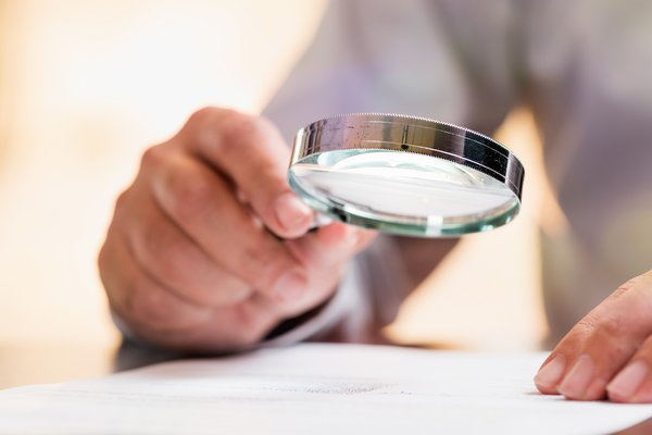 A person uses a magnifying glass to thoroughly examine financial documents.