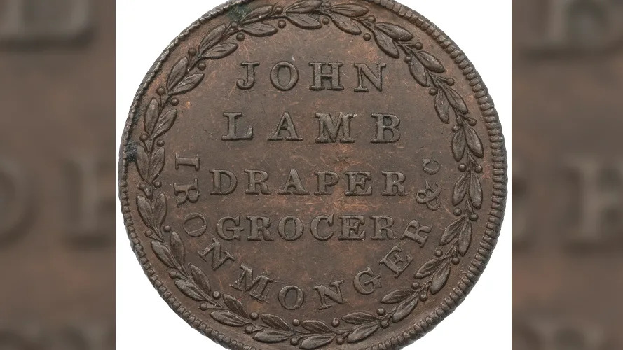 An old copper coin well-preserved with leaves round the edge and in the middle declaring it is from 'John Lamb: draper, grocer, ironmonger'