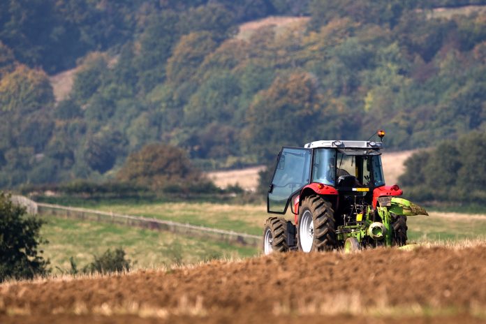 Tractor ploughing a field with a forest in the distance