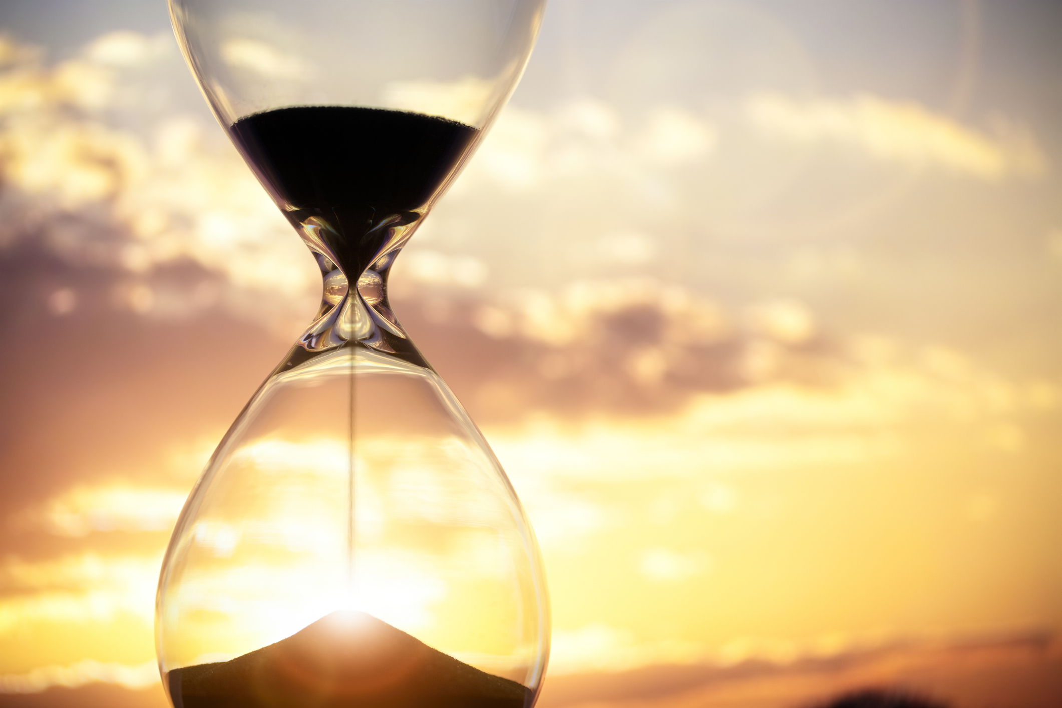 A modern hourglass with the sunset behind it.