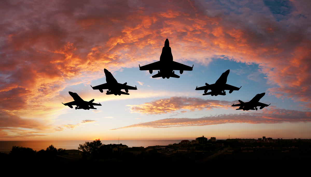 A group of fighter jets fly in formation at sunset.