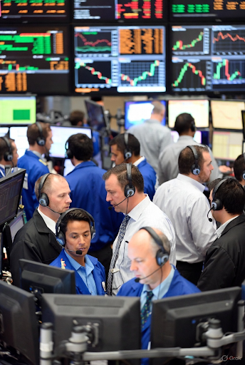 Traders working on a busy stock exchange floor surrounded by monitors showing market charts and financial data — representing global market volatility, stock trading activity, and investor reactions to UK leadership and economic news.
