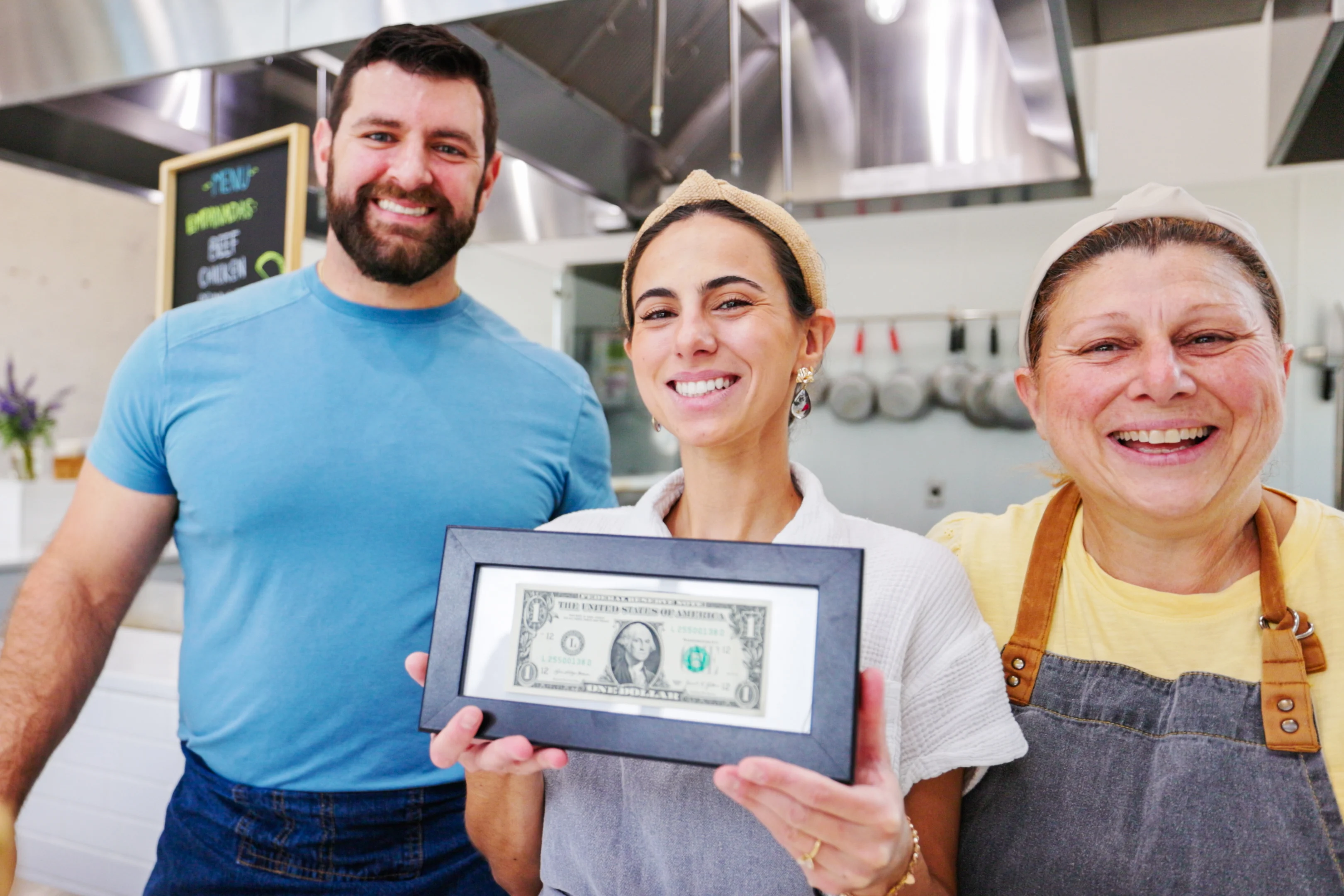 Three individuals hold up a framed dollar bill.