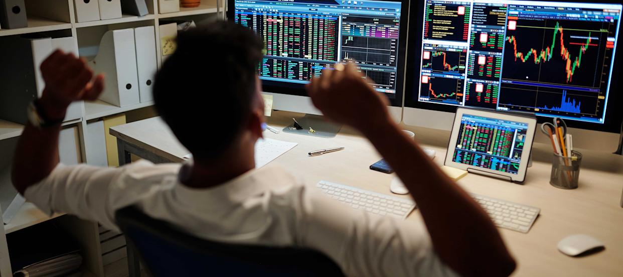 A photo of a day trader looking at investment market data on various screens