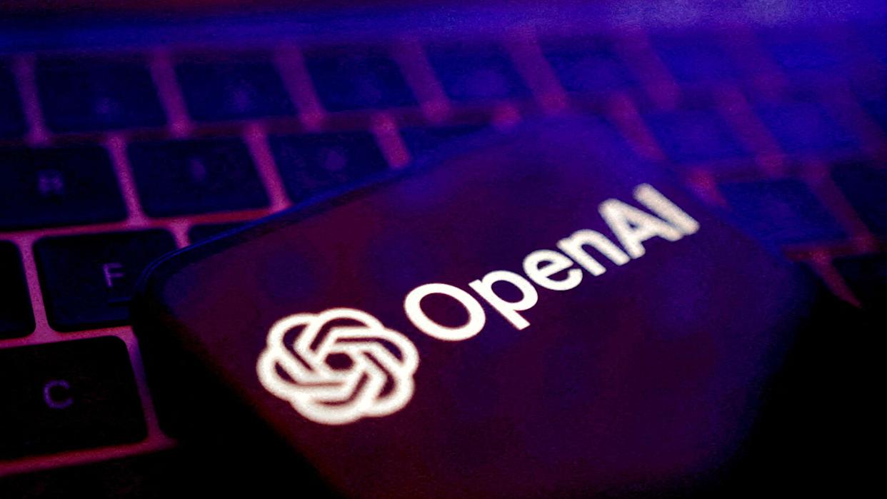 OpenAI logo displayed on a smartphone on top of a laptop keyboard.