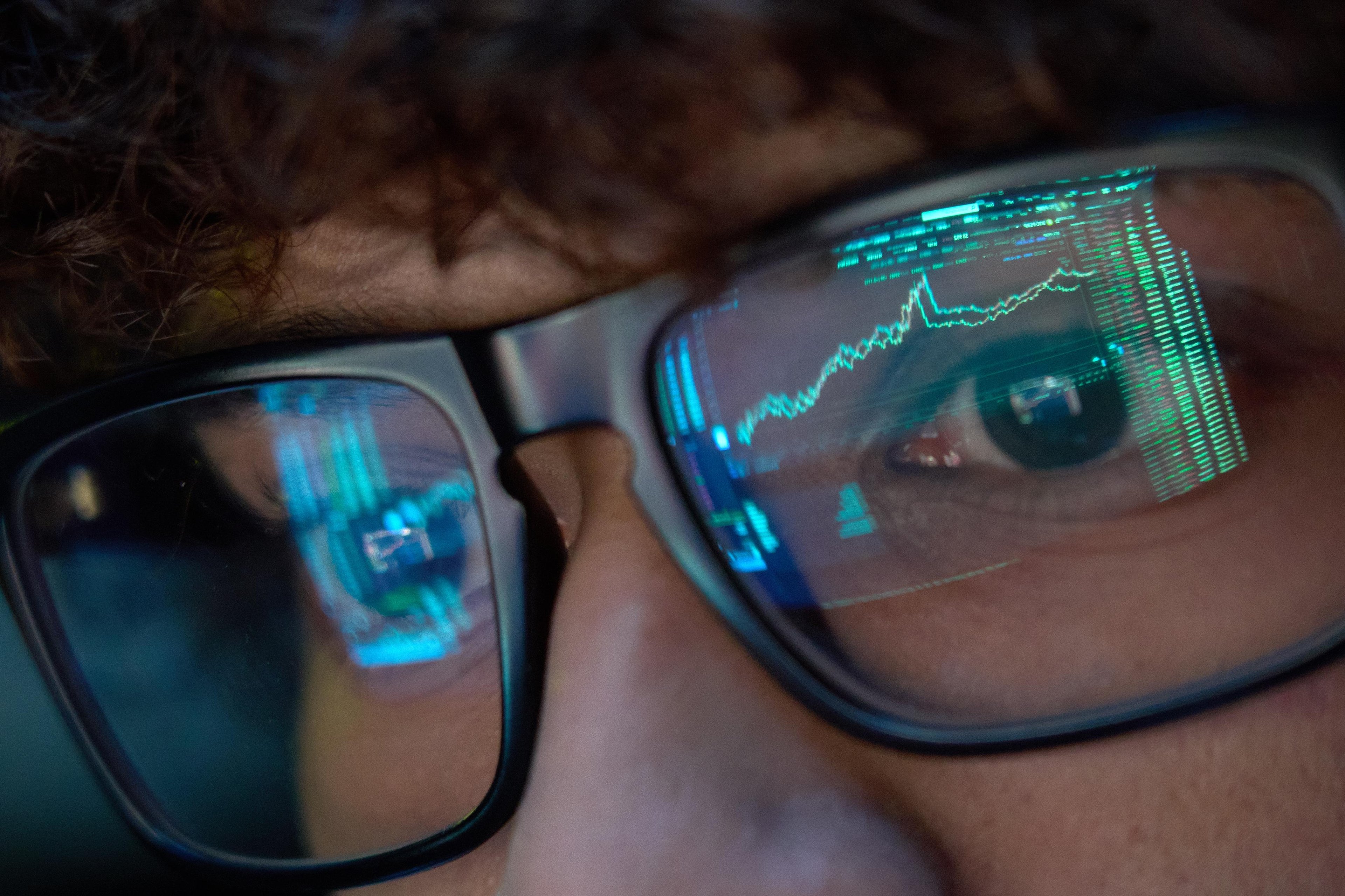 Person wearing glasses with stock market charts and data reflected in the lenses