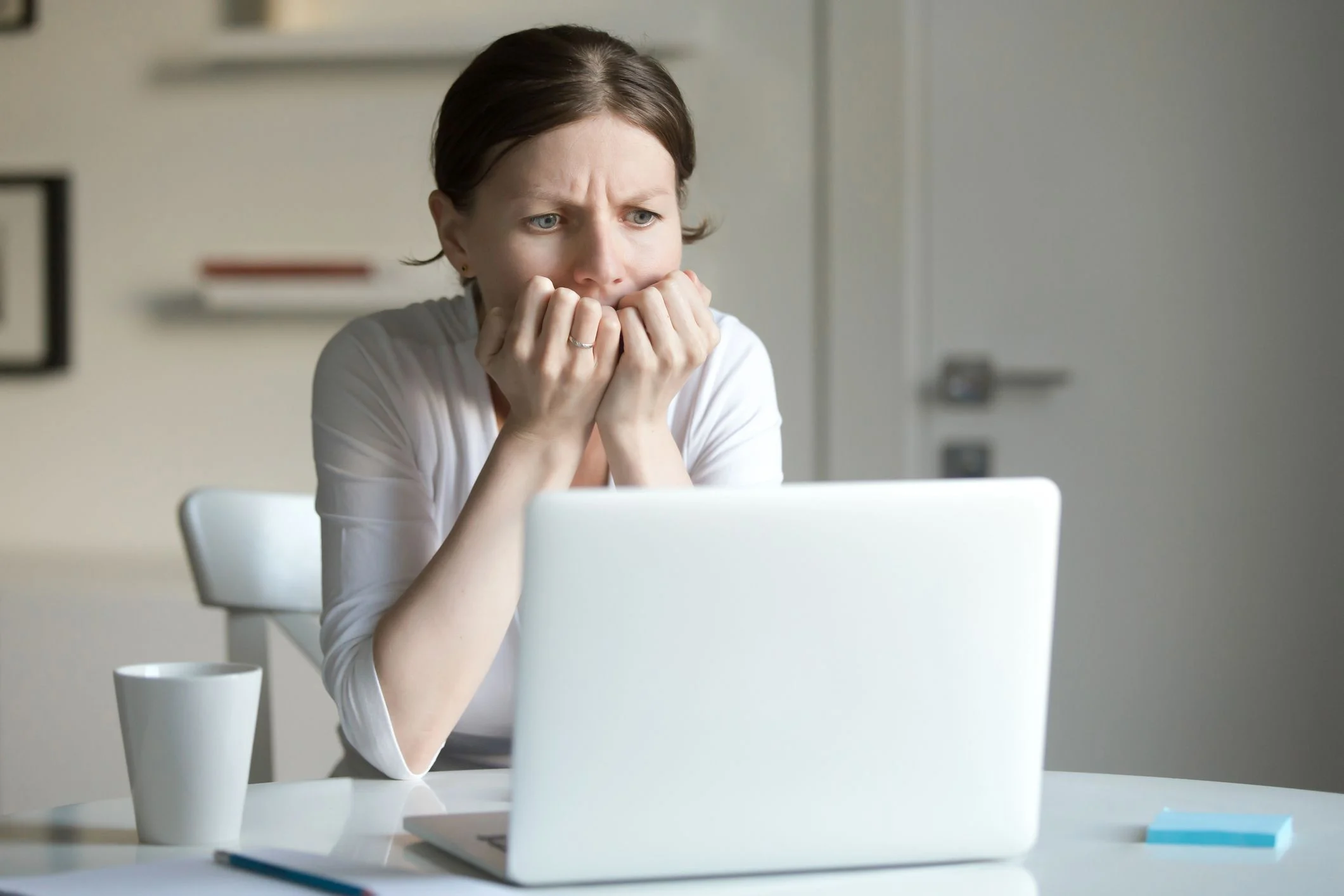 A person looks at a laptop with a worried expression on their face.