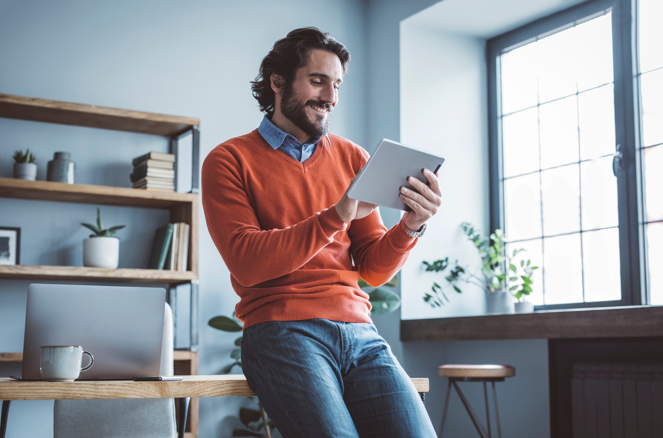 An investor leans against a desk and looks at something on a tablet.