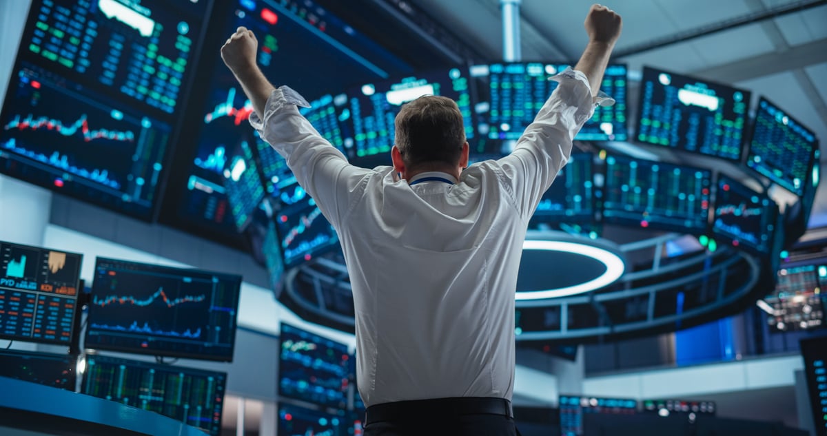 Person cheering in a stock exchange with stock charts.