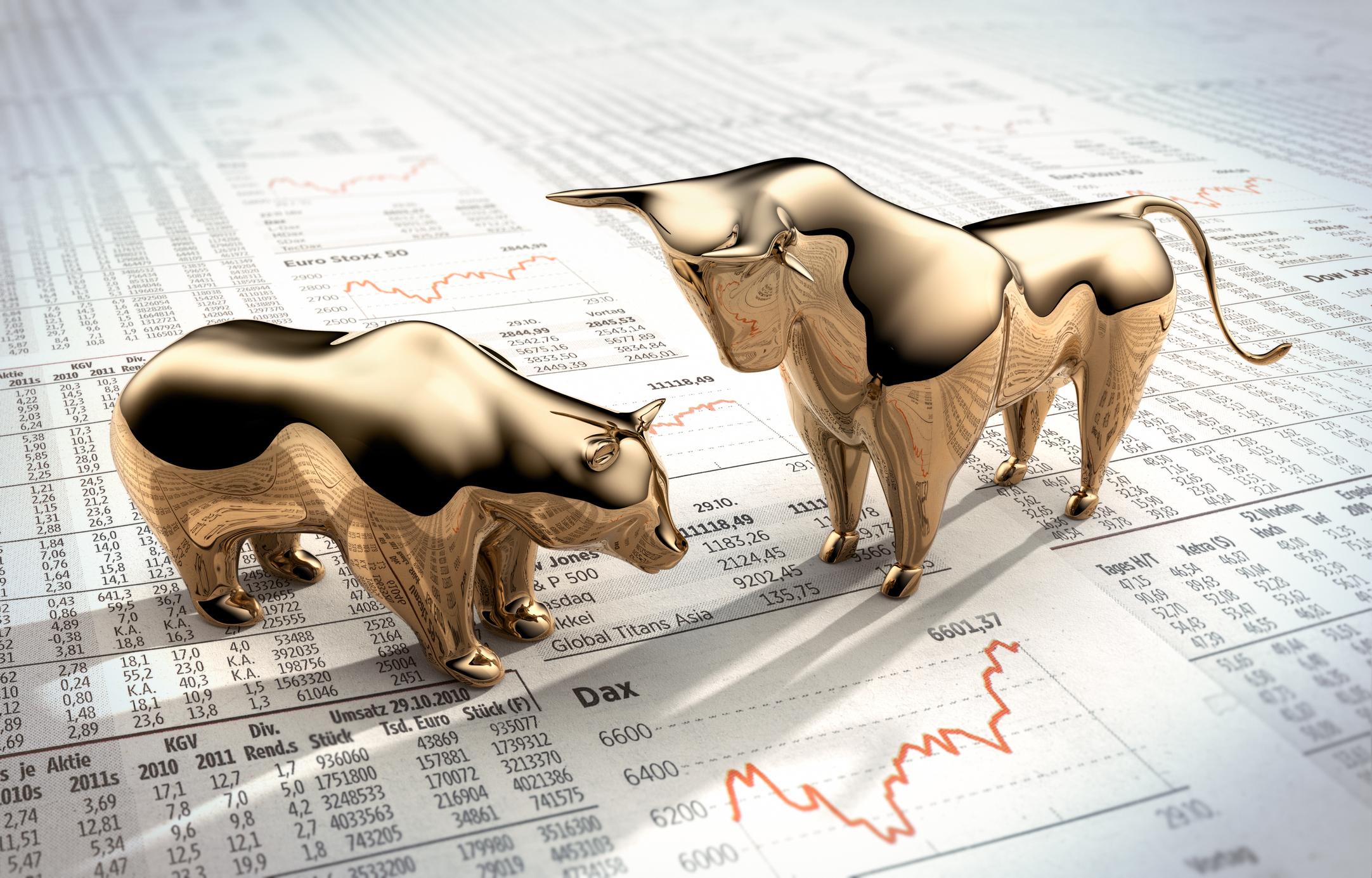 Golden bull and bear figurines on financial market charts symbolize stock market trends.